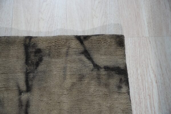 A textured brown and black abstract rug edge rests on light blonde wood flooring.