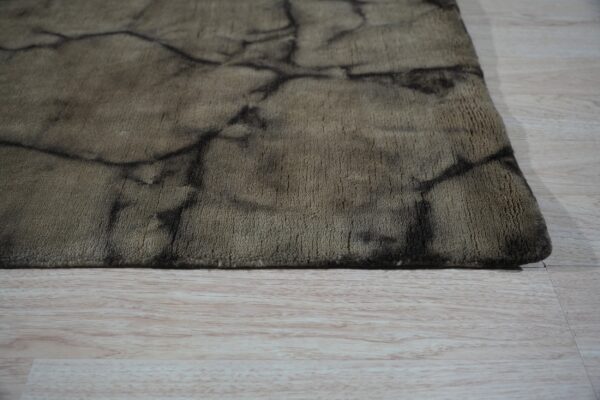 A taupe short-pile rug with a dark abstract cracked pattern rests on light wood flooring.