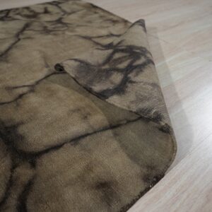 Brown rug with a dark vein pattern is folded on light wood flooring.