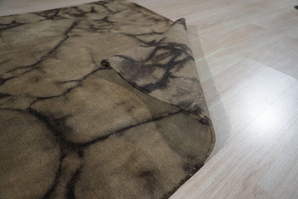 Brown rug with a dark vein pattern is folded on light wood flooring.