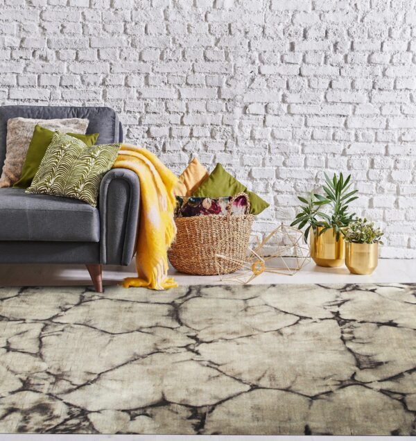 Light-colored rug with a dark crackle pattern anchors a gray sofa against a textured white brick wall.
