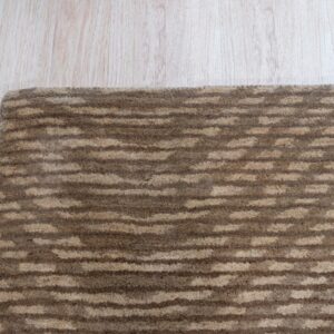 Brown and beige textured striped rug corner placed on pale blonde wood flooring.