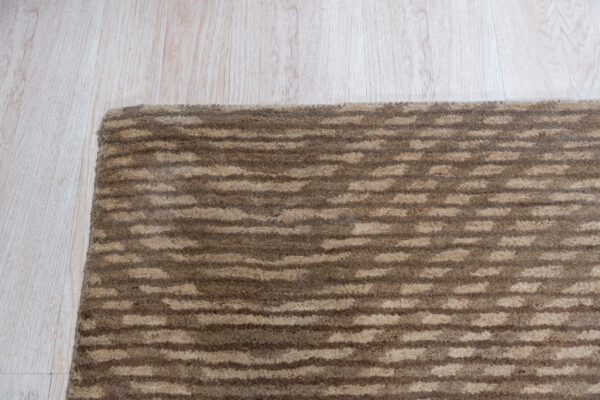 Brown and beige textured striped rug corner placed on pale blonde wood flooring.