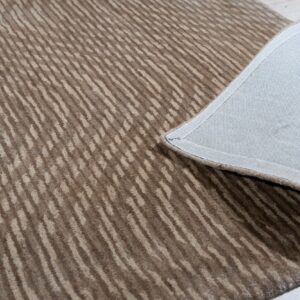 Medium-pile brown and beige rug with organic stripes folded back, revealing the gray backing on light wood floors.