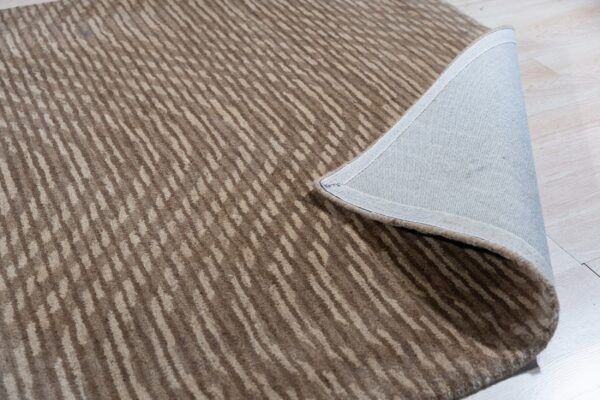 Medium-pile brown and beige rug with organic stripes folded back, revealing the gray backing on light wood floors.