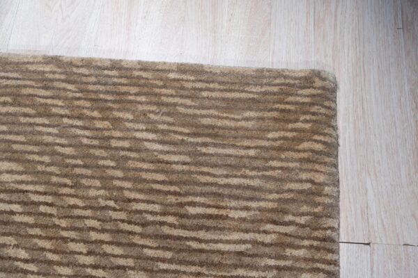 Close-up of a textured brown rug with horizontal stripe pattern on light wood plank flooring.