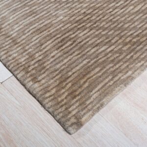 Textured beige and brown striped rug corner rests on light blonde wood flooring.