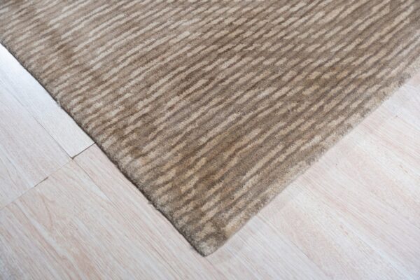 Textured beige and brown striped rug corner rests on light blonde wood flooring.
