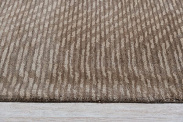 Textured beige rug with irregular vertical stripe patterns in contrasting dark and light brown tones on wood floor.