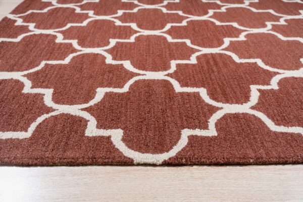 Close-up of a rust brown textured rug with a repeating off-white quatrefoil pattern on light wood flooring.