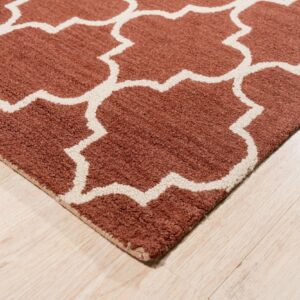A textured rust rug featuring an off-white geometric pattern lies on light-colored wood flooring.