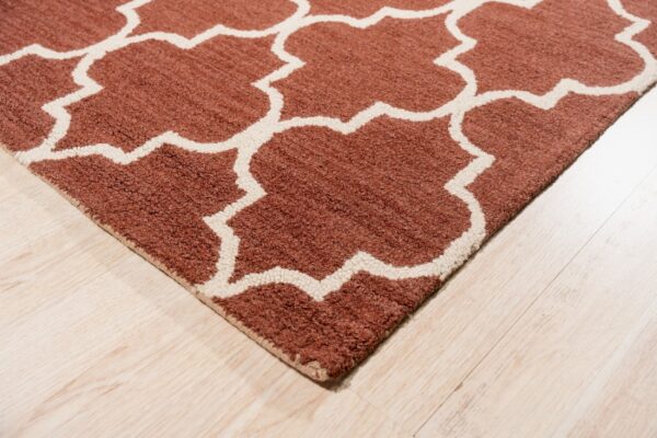 A textured rust rug featuring an off-white geometric pattern lies on light-colored wood flooring.