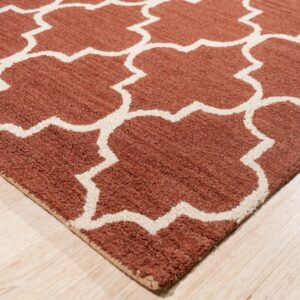 A textured terracotta and white geometric rug sits angled on light wood plank flooring.