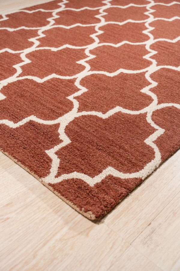 A textured terracotta and white geometric rug sits angled on light wood plank flooring.