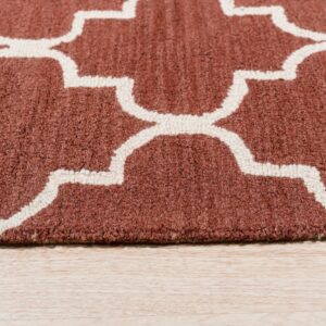 A close-up of a rust rug with a cream geometric trellis pattern on light wood flooring.