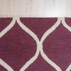 Burgundy textured rug featuring a cream geometric trellis pattern on light blonde wood flooring.