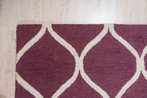 Burgundy textured rug featuring a cream geometric trellis pattern on light blonde wood flooring.