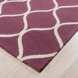A purple rug with a cream geometric trellis pattern rests on light blonde wood flooring.