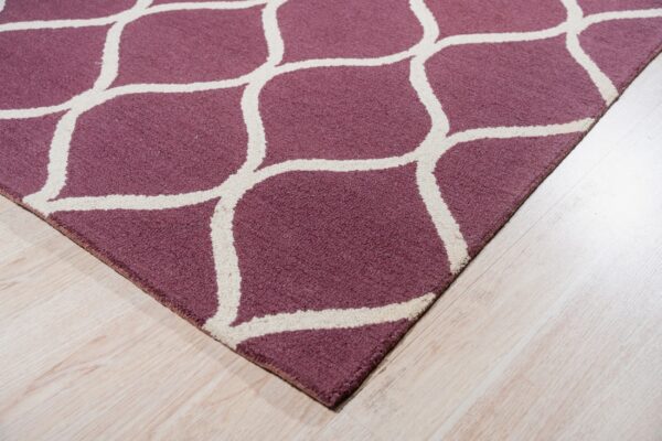 A purple rug with a cream geometric trellis pattern rests on light blonde wood flooring.