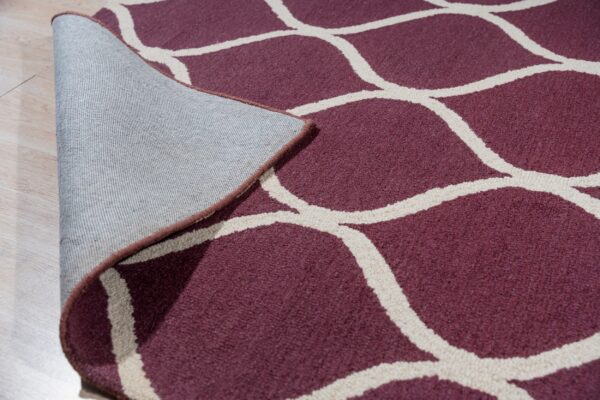 Low-pile maroon rug with a cream geometric pattern is lifted, showing the gray woven backing on light wood floor.