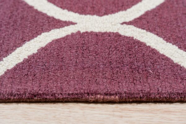 Textured maroon rug with intersecting cream lines rests on light natural wood flooring.