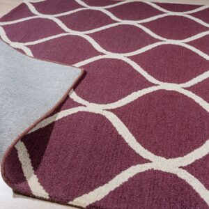 Close-up of a maroon rug with a cream trellis pattern, folded back revealing the textile backing.