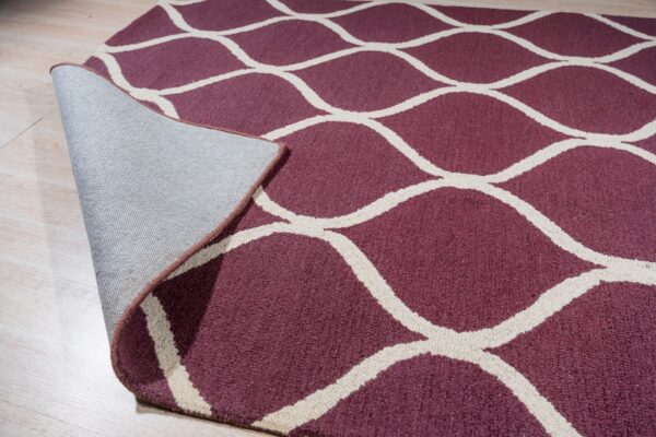 Close-up of a maroon rug with a cream trellis pattern, folded back revealing the textile backing.