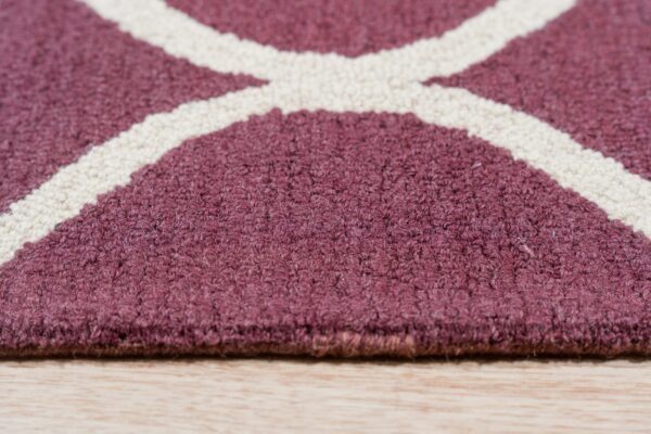 Close view of a looped maroon and cream rug with a geometric pattern on light wood floor.