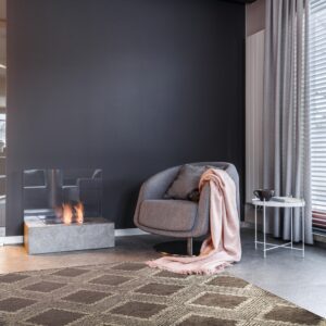 Dark brown rug with a repeating geometric diamond pattern anchors a modern room with a gray chair and fireplace.