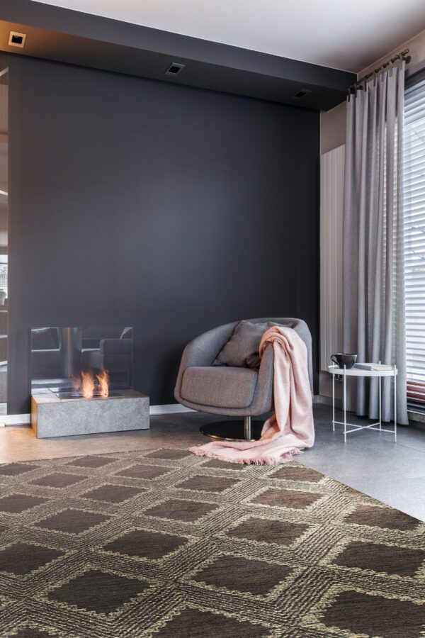 Dark brown rug with a repeating geometric diamond pattern anchors a modern room with a gray chair and fireplace.