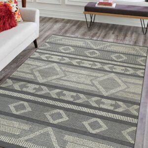 A dark gray and cream flatweave rug with geometric bands rests on gray wood floors by a window.