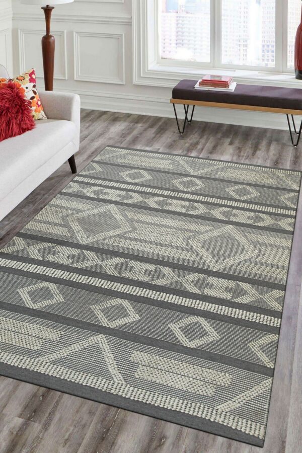 A dark gray and cream flatweave rug with geometric bands rests on gray wood floors by a window.
