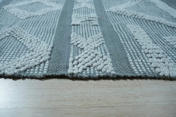 Textured gray rug with raised off-white diamond patterns and woven vertical stripes on light wood.