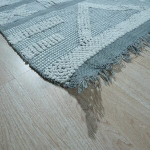 Textured gray and white rug featuring a raised geometric pattern and fringe on pale wood floor.