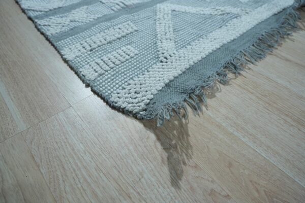 Textured gray and white rug featuring a raised geometric pattern and fringe on pale wood floor.