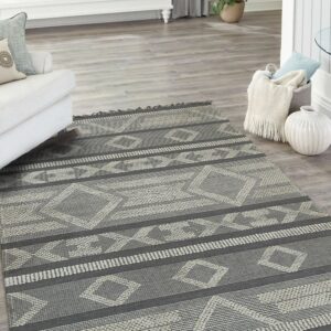 Low-pile charcoal and light gray geometric rug with tassel fringe sits in a bright living room.