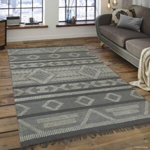 Gray low-pile geometric rug with fringe rests on wood flooring beside a gray couch.