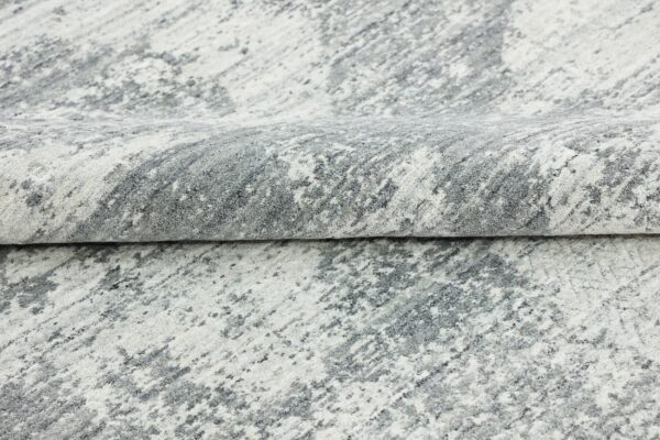 Abstract patterned high-pile rug folded, featuring shades of white and mottled gray.