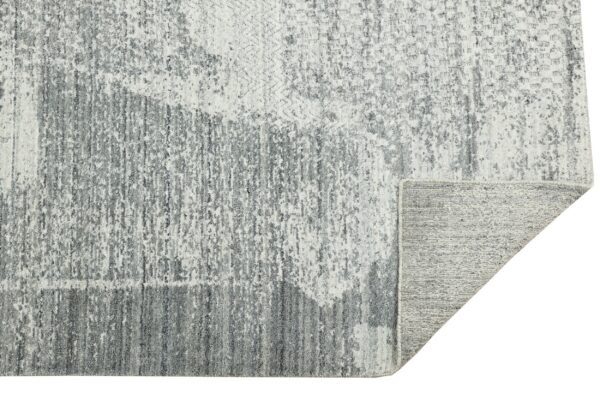Abstract gray and white textured rug features distressed vertical lines; a corner is folded showing the woven backing.
