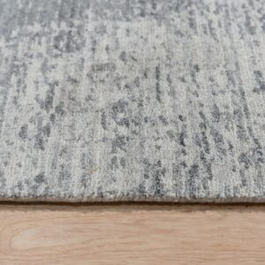 Medium pile rug in gray and white abstract pattern rests on natural wood floorboards.
