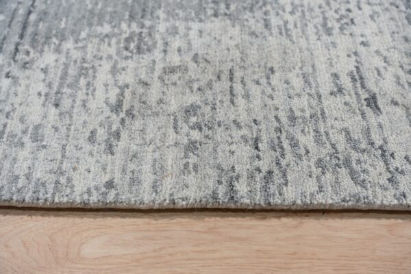 Medium pile rug in gray and white abstract pattern rests on natural wood floorboards.