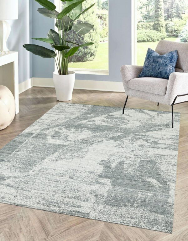 Distressed gray and white abstract rug sits on chevron wood flooring between a large plant and a light gray armchair.