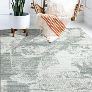 A low-pile, abstract gray and white rug sits under a wicker chair and a tall potted plant.