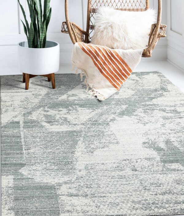 A low-pile, abstract gray and white rug sits under a wicker chair and a tall potted plant.