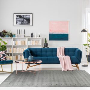 Gray rug with subtle texture and dotted border under a rose gold table and blue velvet sofa.