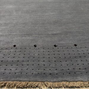 Dark gray textured rug with dark dotted pattern near the edge, long tan fringe, resting on wood floor.
