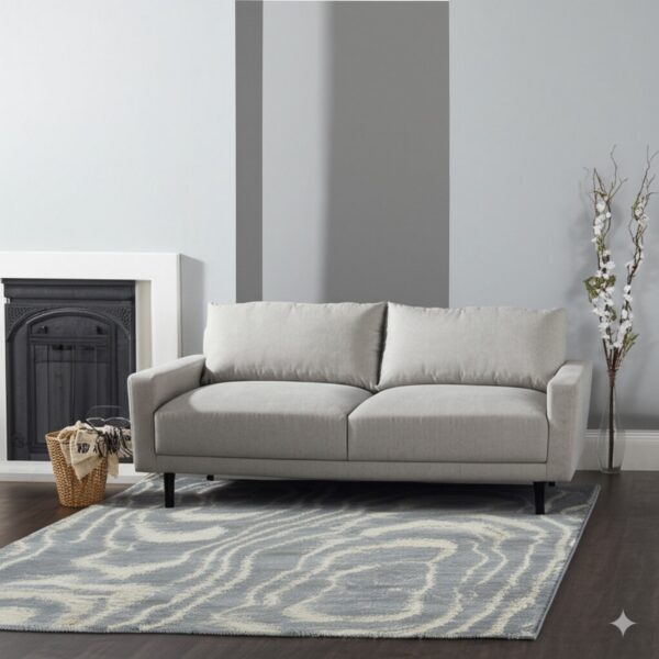 A low-pile blue and cream wave-patterned rug sits on a dark wood floor beneath a light gray sofa.