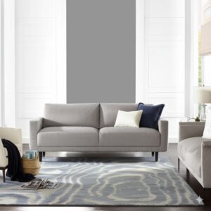 A low-pile blue and white abstract rug anchors a modern gray sofa on dark wood flooring.