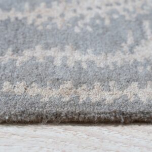 Close-up shows the thick pile of a gray and cream abstract patterned rug on light wood flooring.