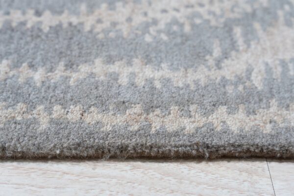 Close-up shows the thick pile of a gray and cream abstract patterned rug on light wood flooring.